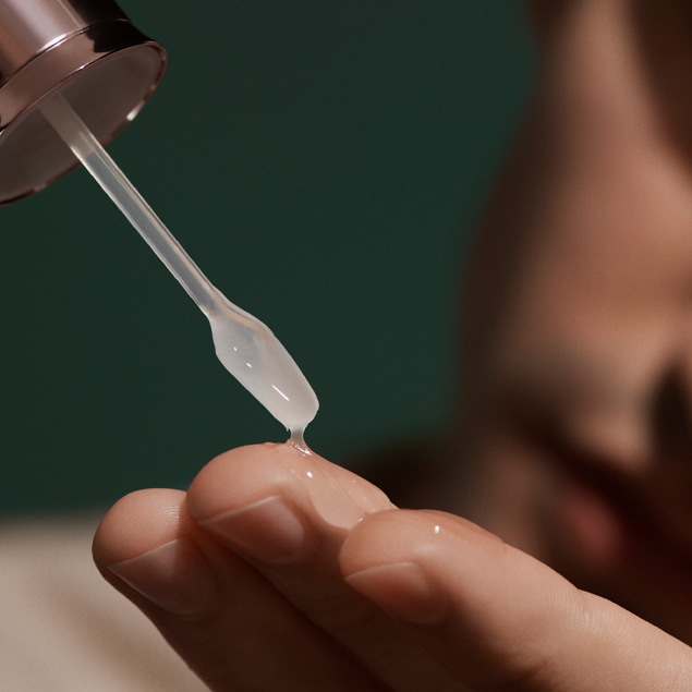 Macro shot of applicator applying serum onto fingertips.