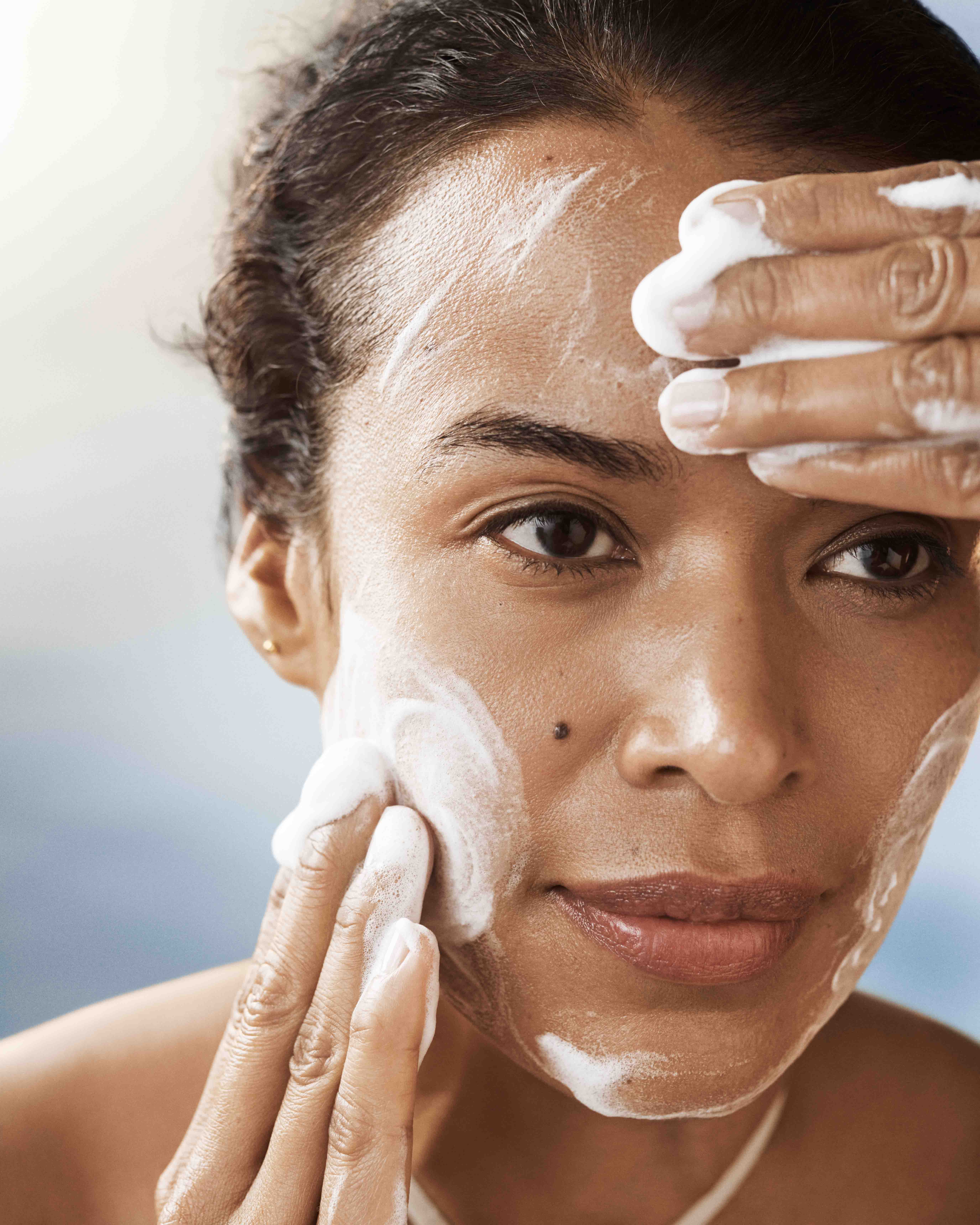 Close up of lady cleansing her face with foam cleanser and foam on her face with two hands on forehead and cheek.