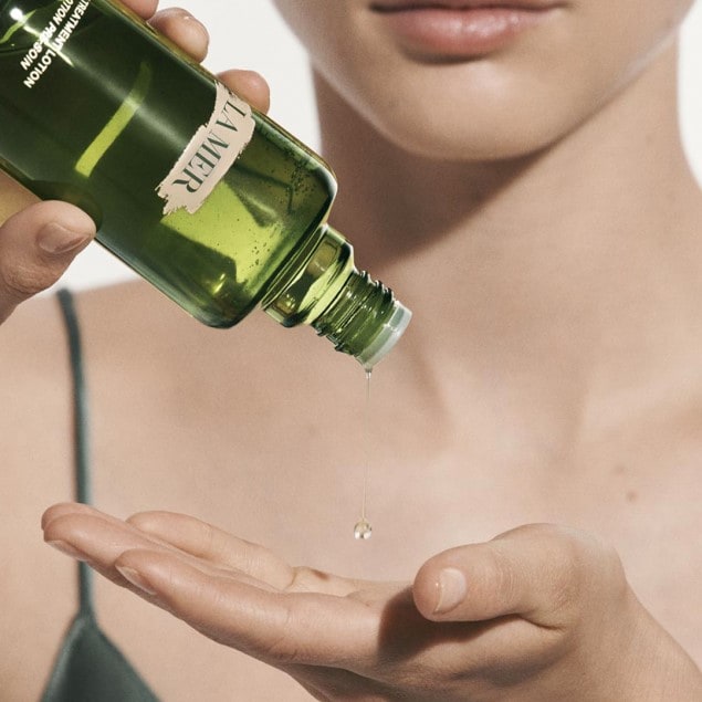 Woman close up of hand holding a bottle of Treatment lotion dripping into her palm.