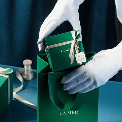 Hands placing gift box in a la mer gift bag - complimentary Gift Wrap